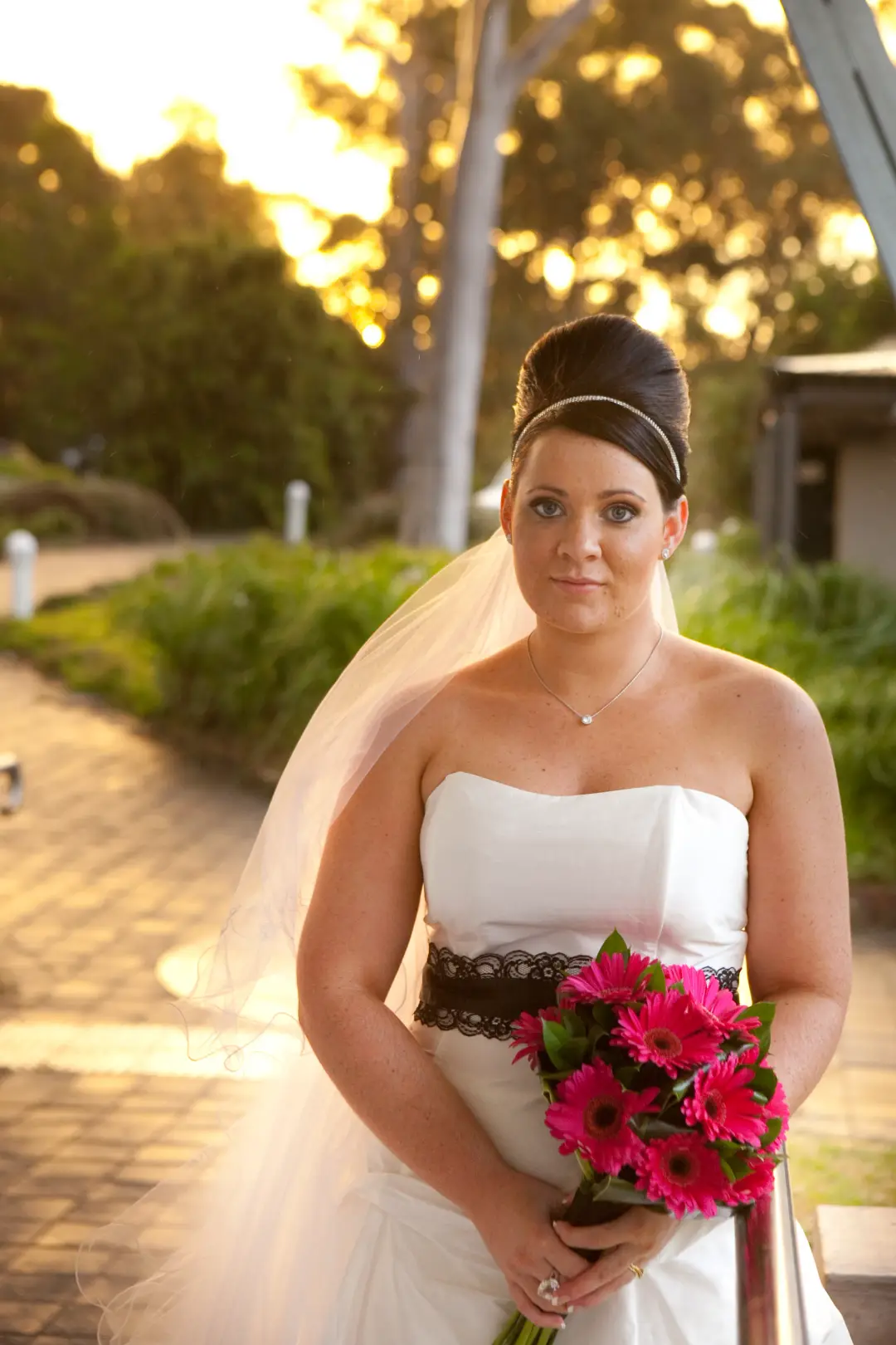 Bride at golden hour in a beehive style with a black band, holding pink gerberas