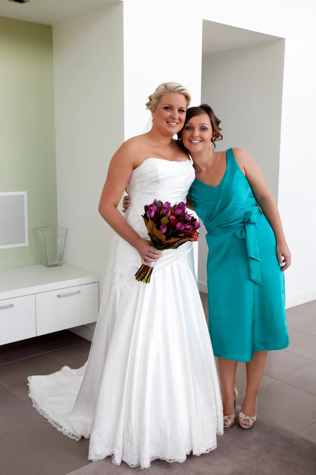 Bride with her bridesmaid in teal, both styled with their hair pinned up