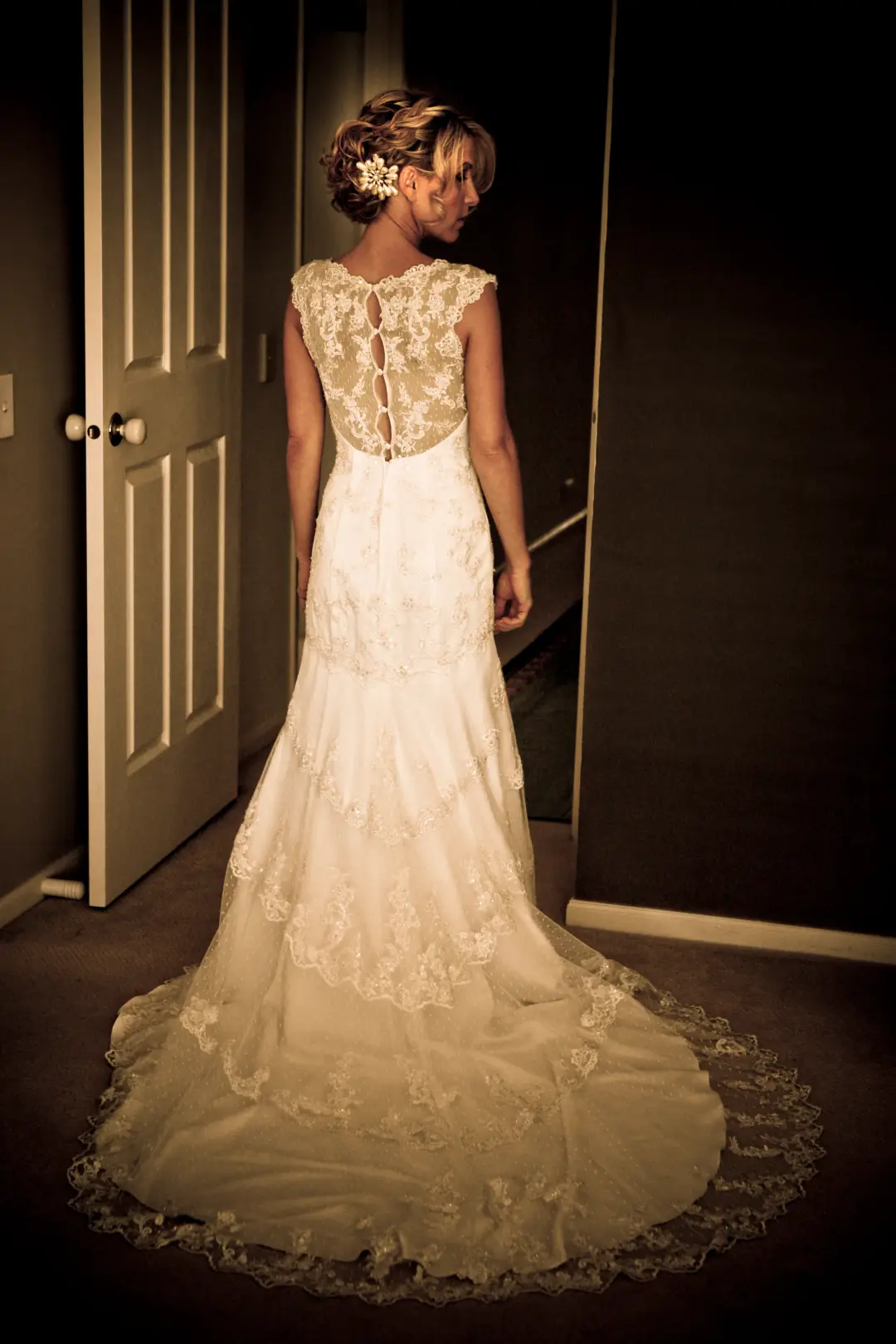 Back of a lace gown with the bride's hair pinned into a low updo dressed with a hairpiece