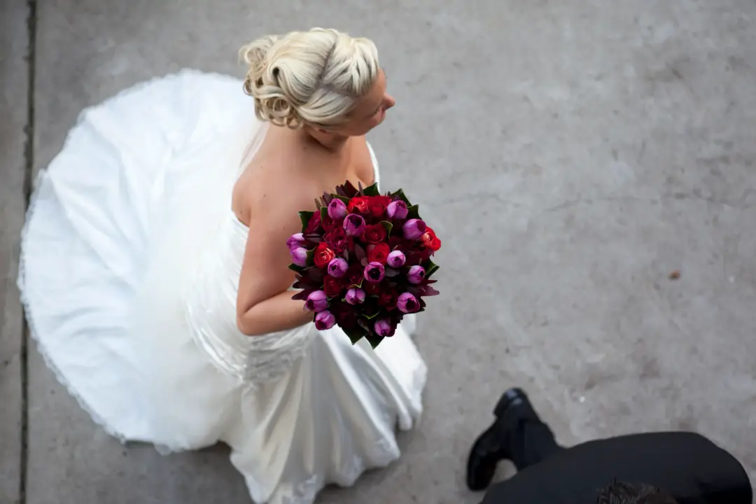 Bride photographed from above holding a deep pink and burgundy bouquet, her blonde hair pinned into a low updo