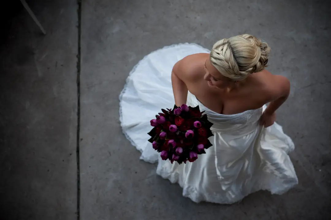 Bride from above holding a deep purple calla bouquet, her blonde hair braided into a low updo
