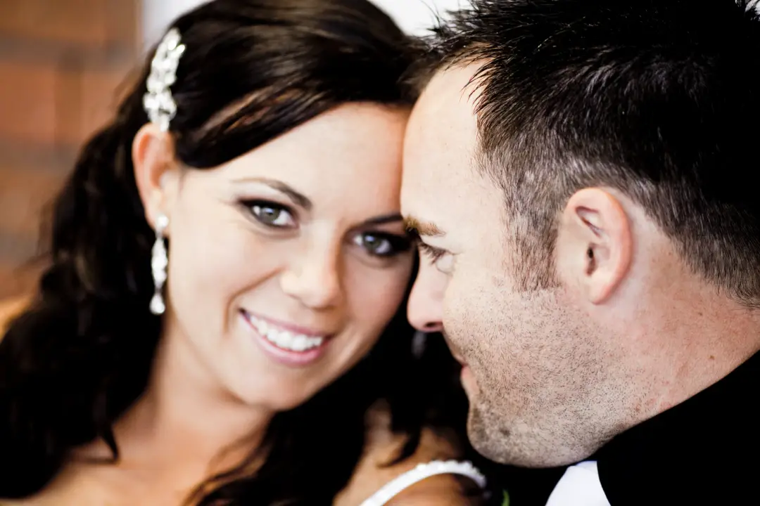 Bride and groom cheek to cheek, her dark hair worn half up with a crystal comb and drop earrings