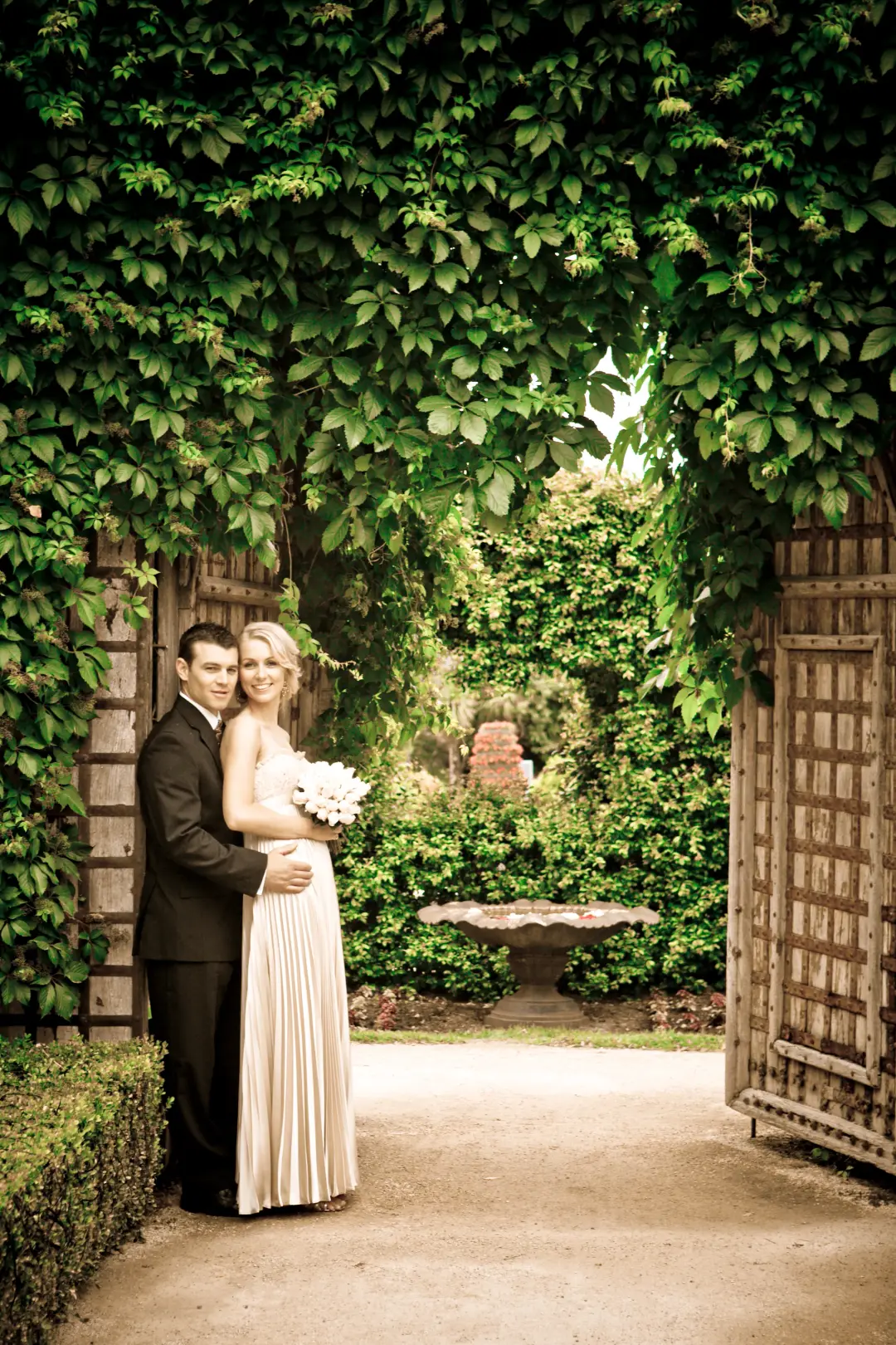 Couple under an ivy archway in a garden, the bride's blonde hair pinned into a soft updo