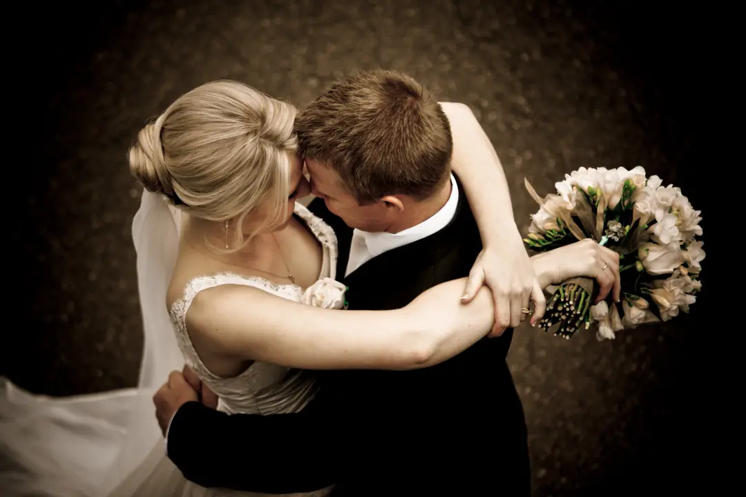 Bride and groom embracing, her blonde hair coiled into a smooth low bun