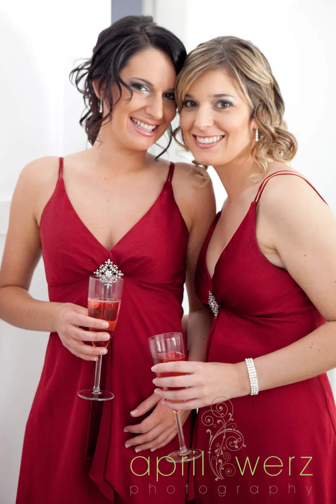 Two bridesmaids in red raising a toast, one with dark hair pinned up and one in blonde curls