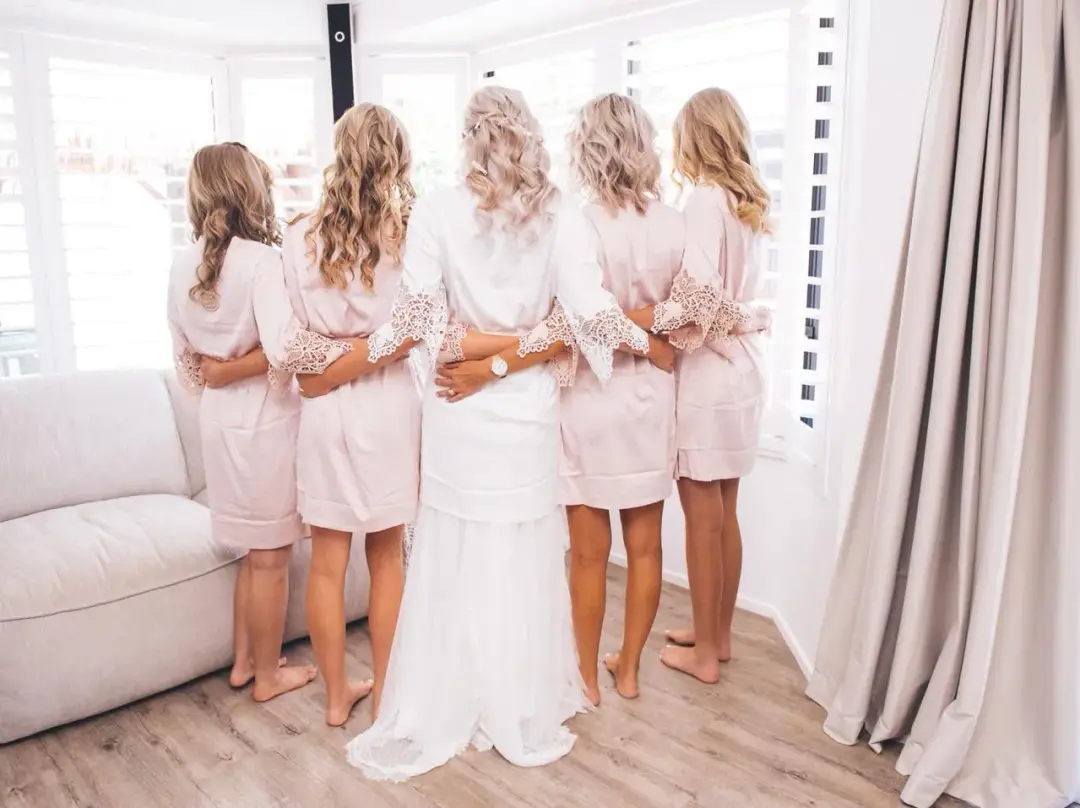 Bride and four bridesmaids in blush robes photographed from behind, every one styled and ready to dress