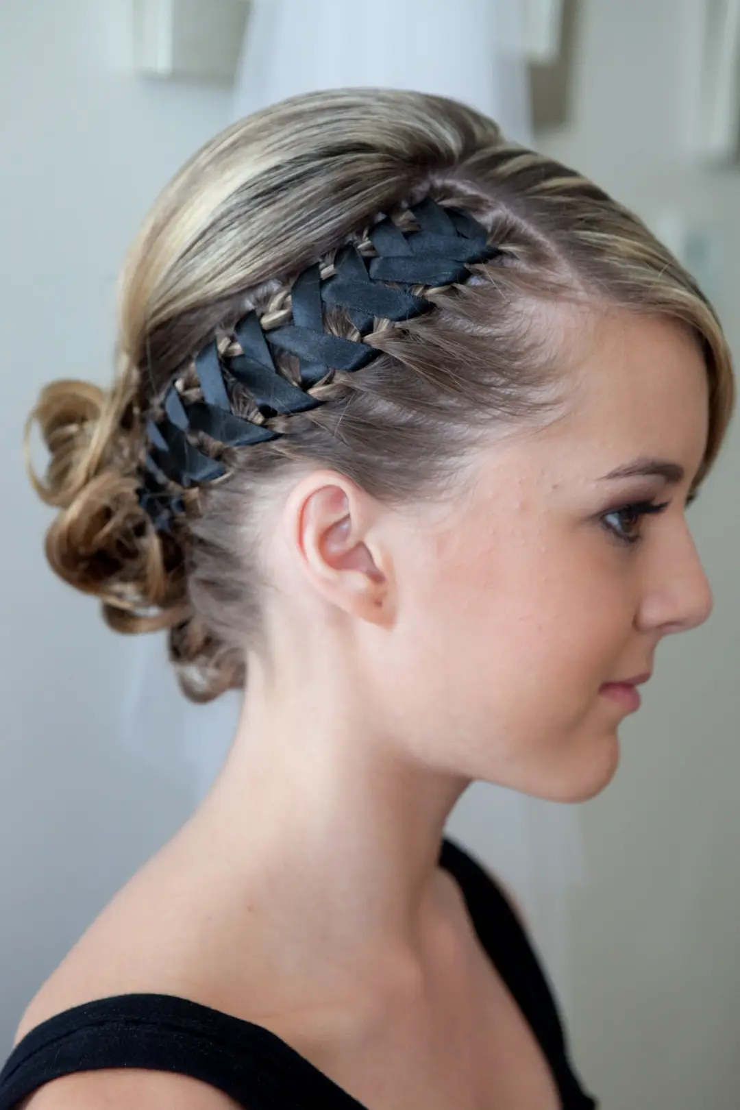 Side view of a ribbon laced through a braid across the crown, finished into a low curled updo