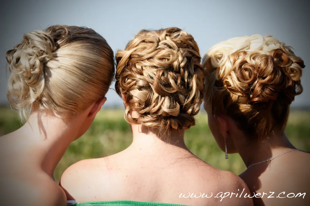 Three bridesmaids photographed from behind, each wearing a different curled updo