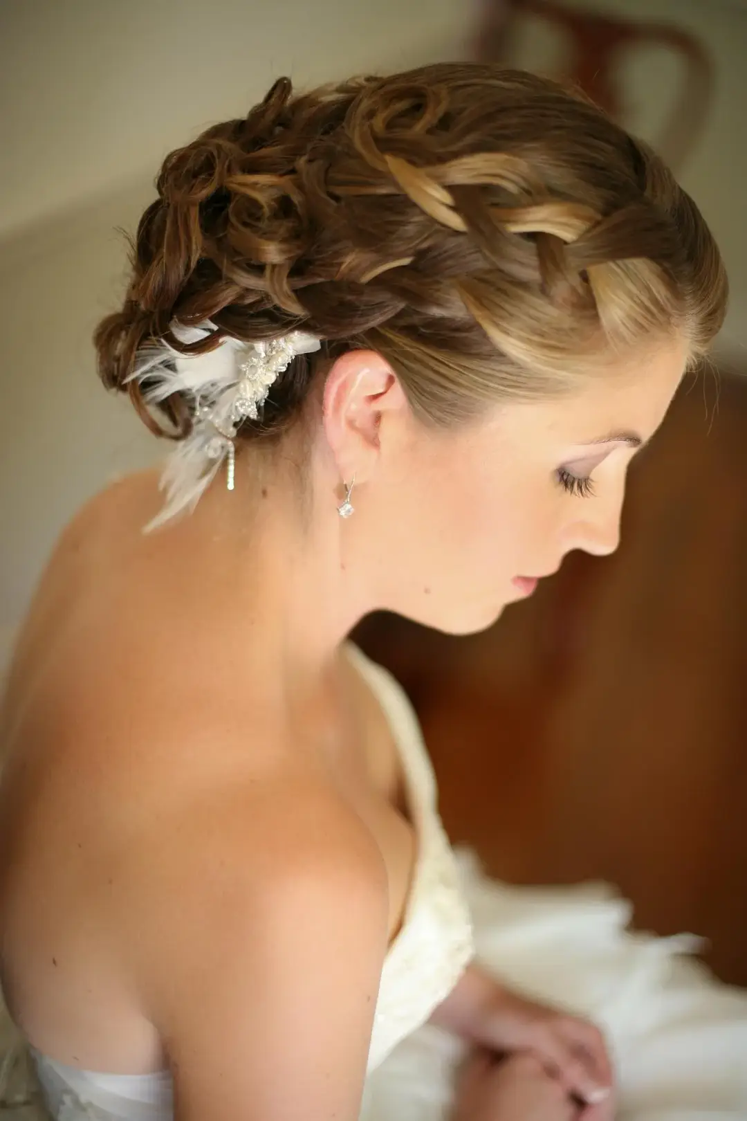 Bride in profile wearing a curled updo dressed with a feather and diamante hairpiece