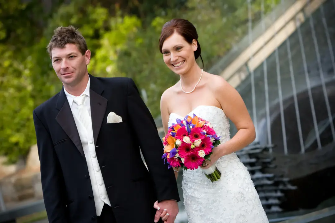 Bride and groom by a fountain, her dark hair pinned back with a bright tropical bouquet