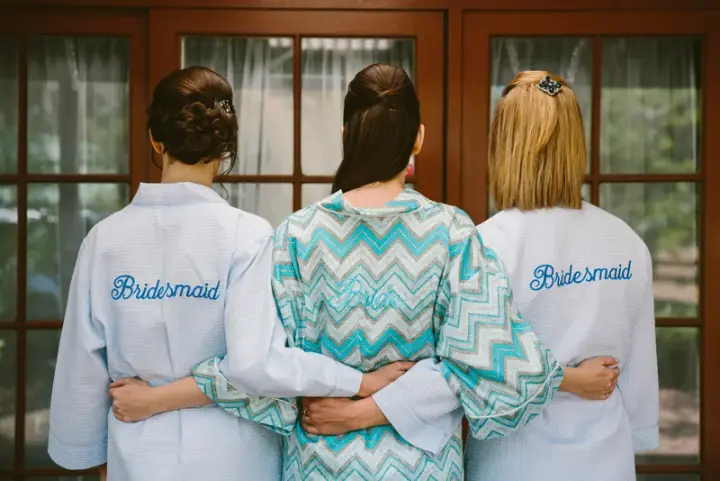 Bride and her two bridesmaids photographed from behind in monogrammed robes, hair styled and ready