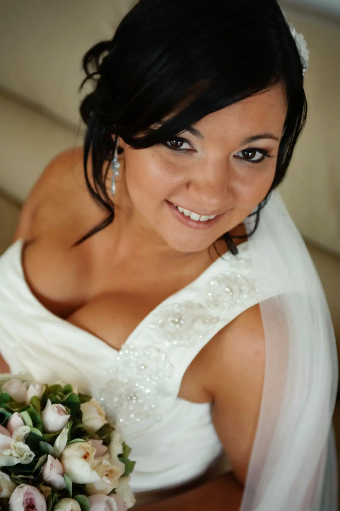 Bride with dark hair pinned into a low updo and a white flower, wearing her veil over one shoulder