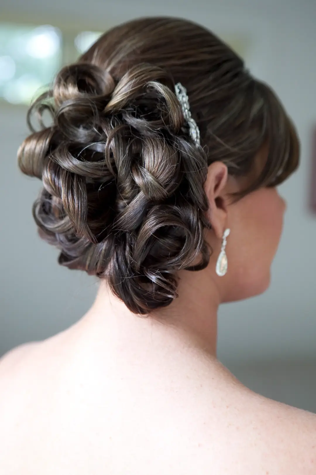 Back view of a full curled brunette updo pinned with a diamante clip and worn with drop earrings