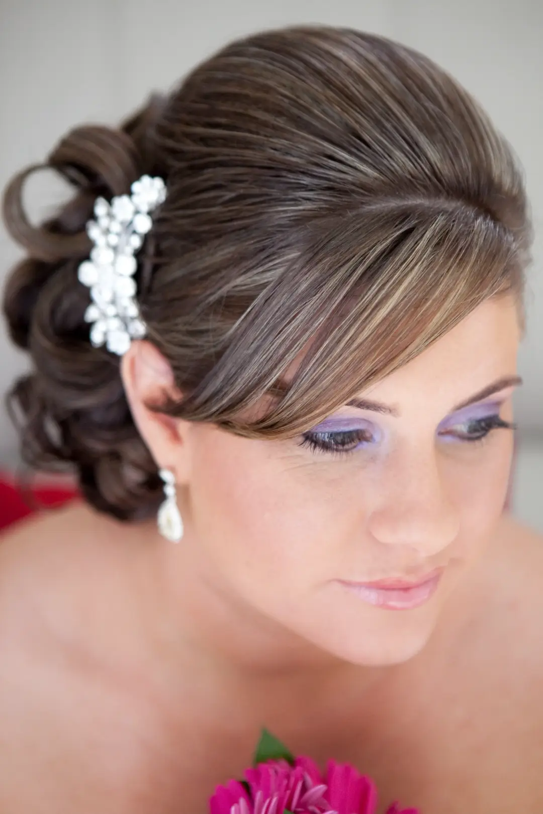 Bride in a sleek side swept updo with a crystal comb and pearl drop earrings, wearing soft lilac eye makeup