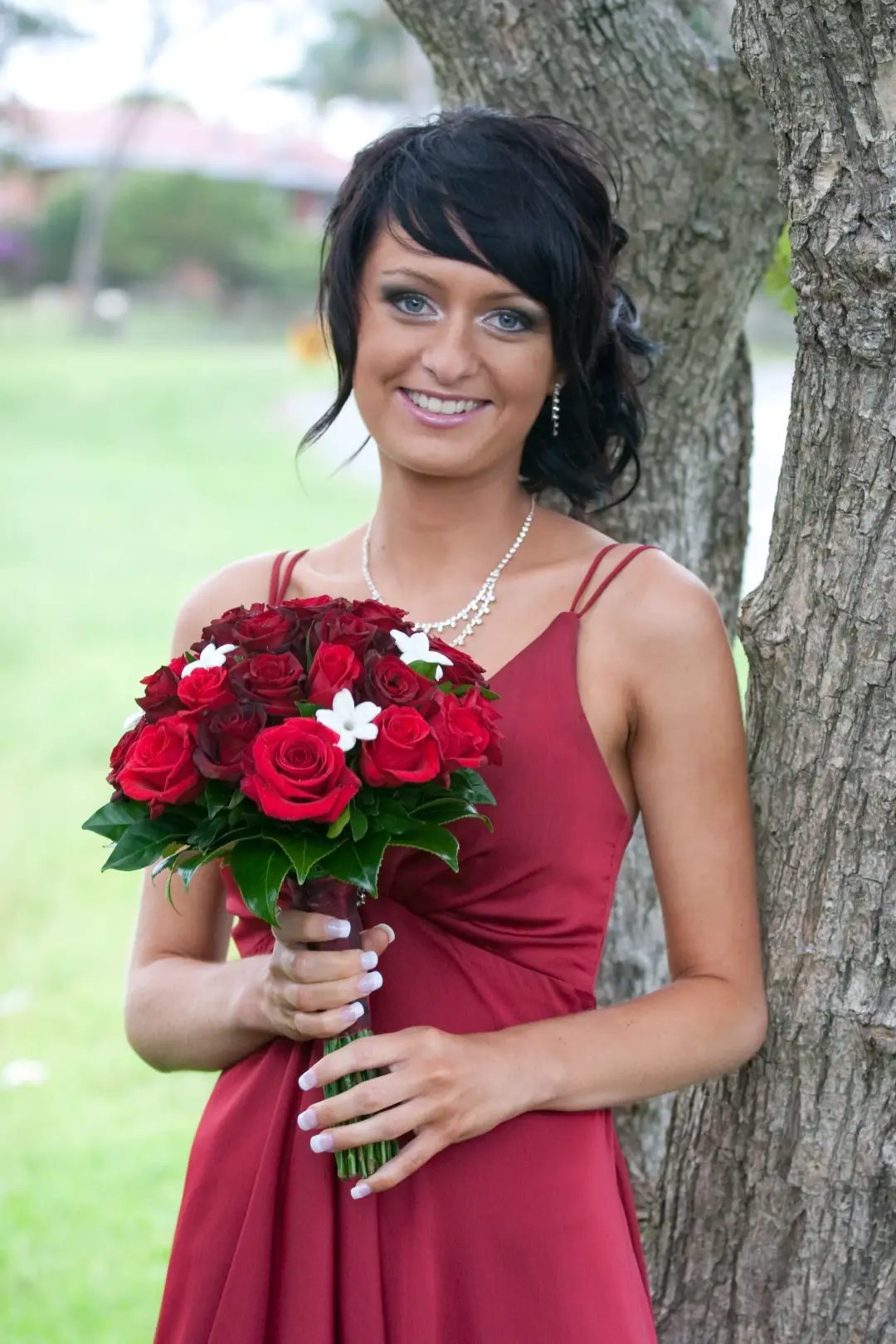 Bridesmaid in a red gown with a dark textured updo and a soft fringe, holding red roses