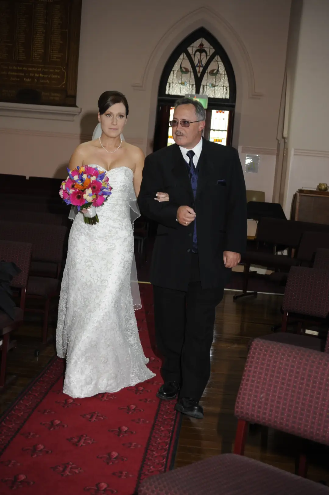 Bride walking up the aisle with her father, her dark hair pinned into a low style