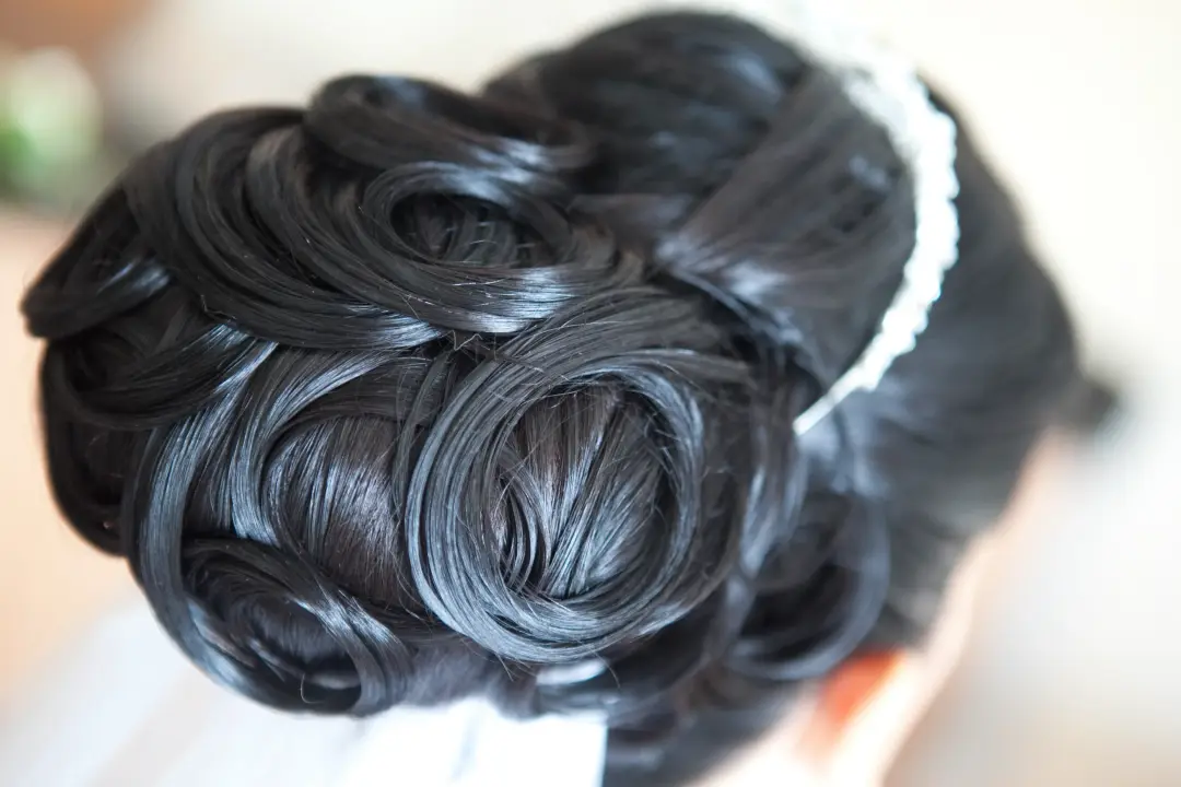 Close view of a dark curled upstyle pinned tightly and finished with a diamante band