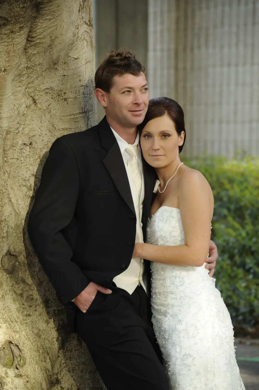 Bride and groom against a tree, the bride's dark hair swept into a smooth low style