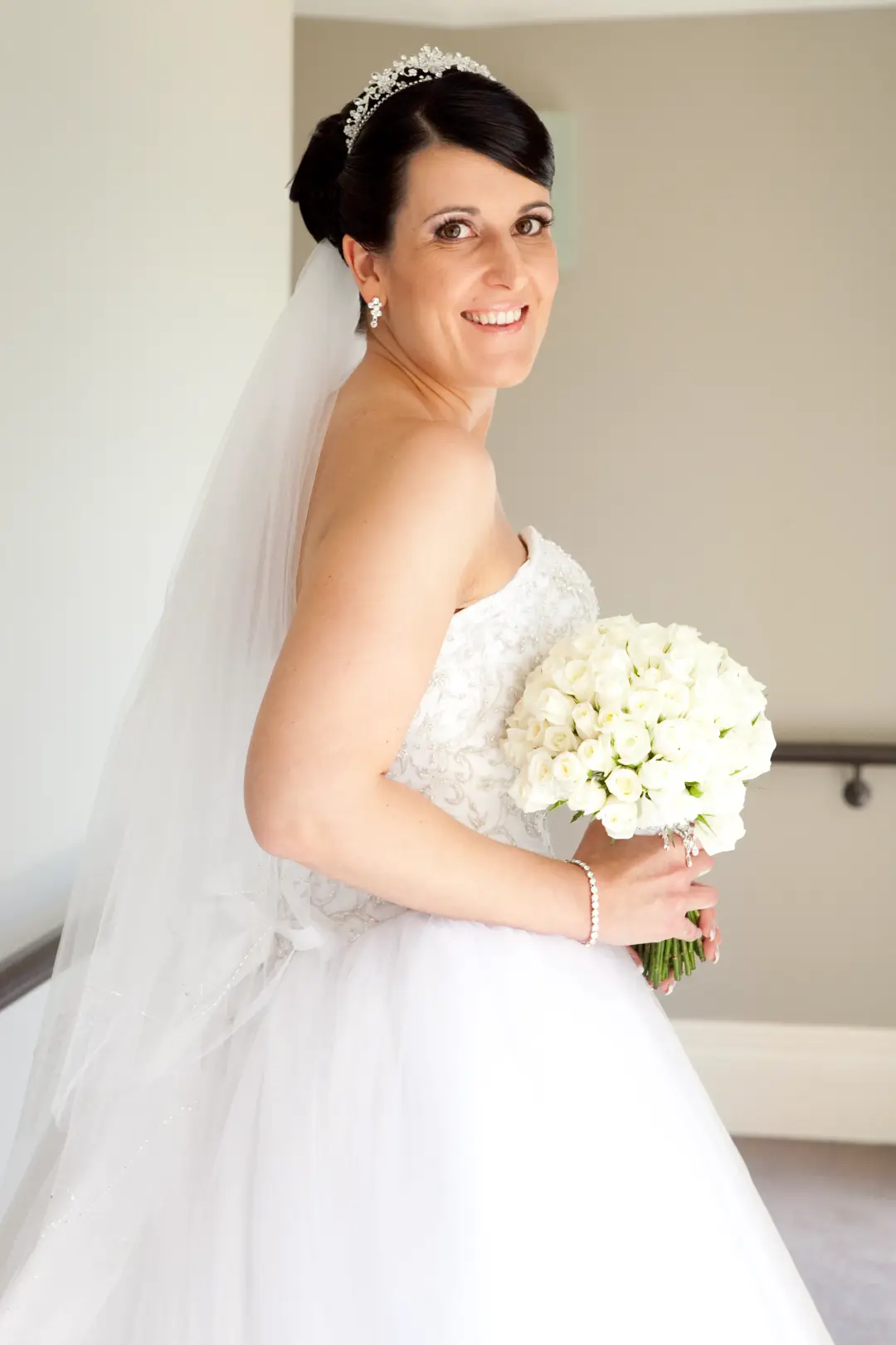 Bride in a tiara and veil with her dark hair pinned into a high updo, holding white tulips