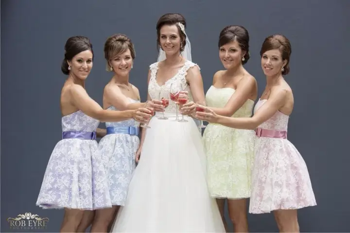 Bride and four bridesmaids raising a toast, every one styled with her hair pinned back
